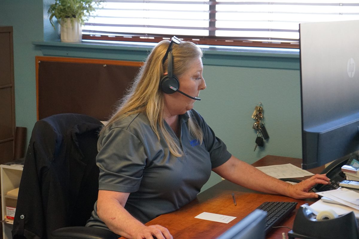Woman wearing a headset works at a desk with a computer monitor in an office