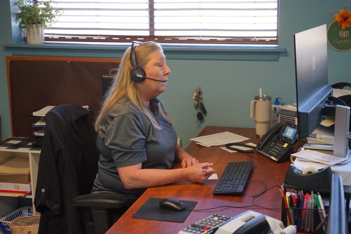 Office worker wearing a headset sits at a desk with a computer and phone
