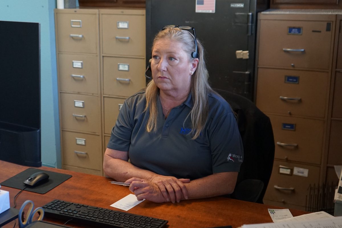 Woman wearing a headset sits at an office desk with filing cabinets and a safe in the background