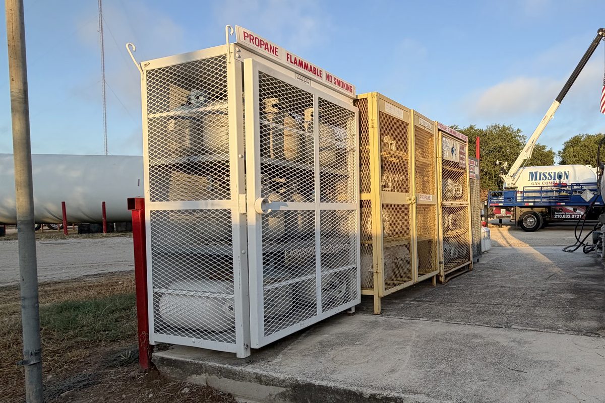 Propane cylinder cages and bulk tanks beside a delivery truck with a crane at the yard