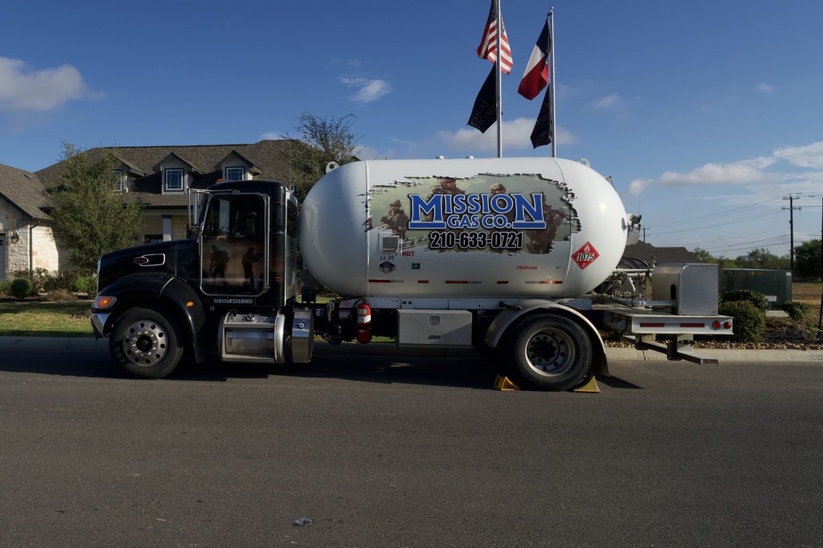 Mission Gas Co. propane delivery truck parked on a residential street with American and Texas flags in the background