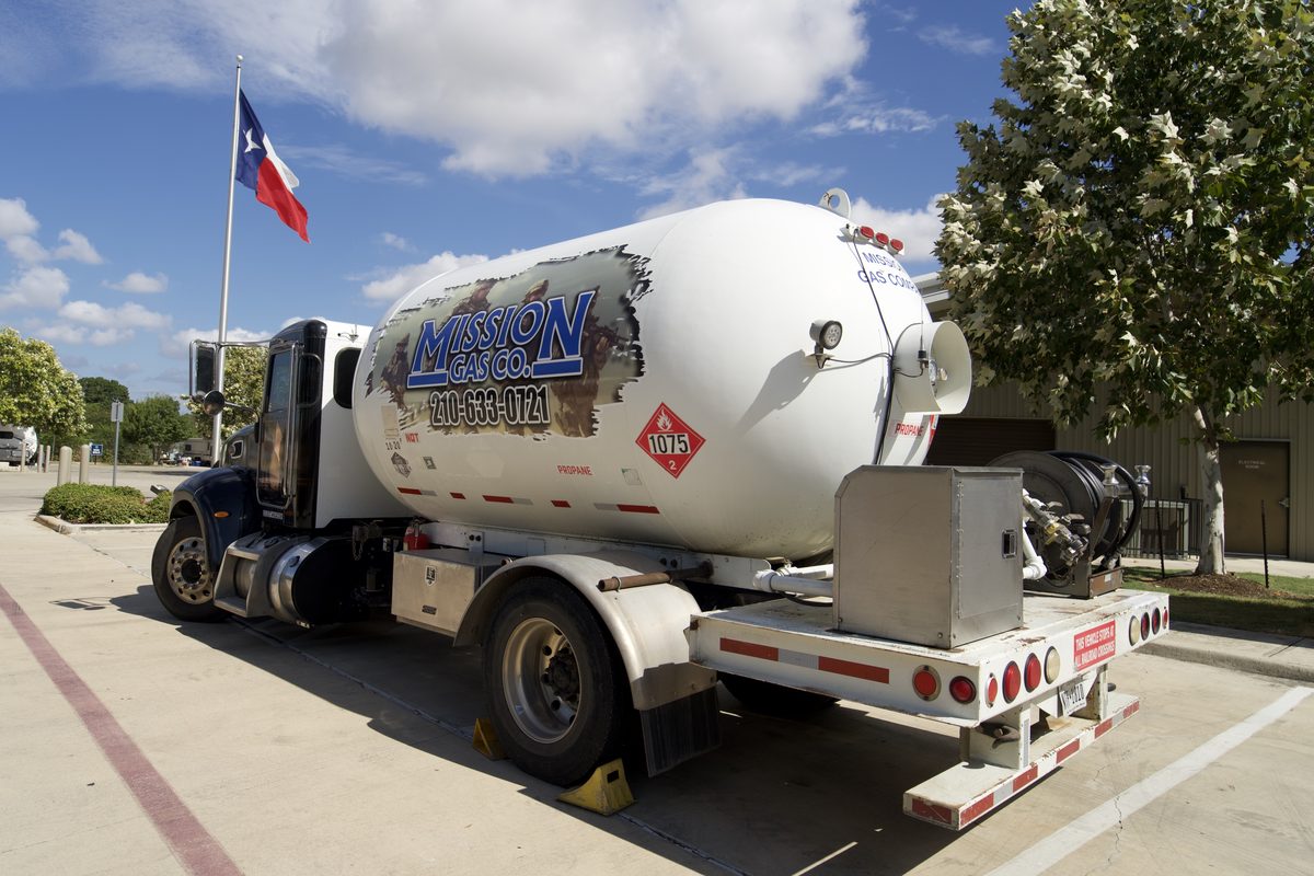 Mission Gas Co. propane delivery truck with large tank, parked near a Texas flag under blue sky