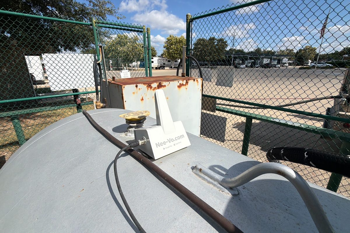 Propane tank top with a Nee-Vo monitor device, fenced yard, and parked RVs in the background