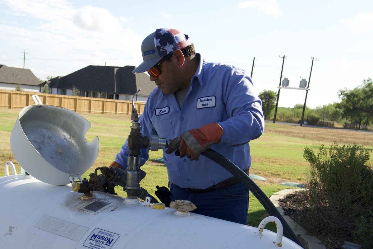 Technician in Mission Gas uniform filling a large propane tank in a yard