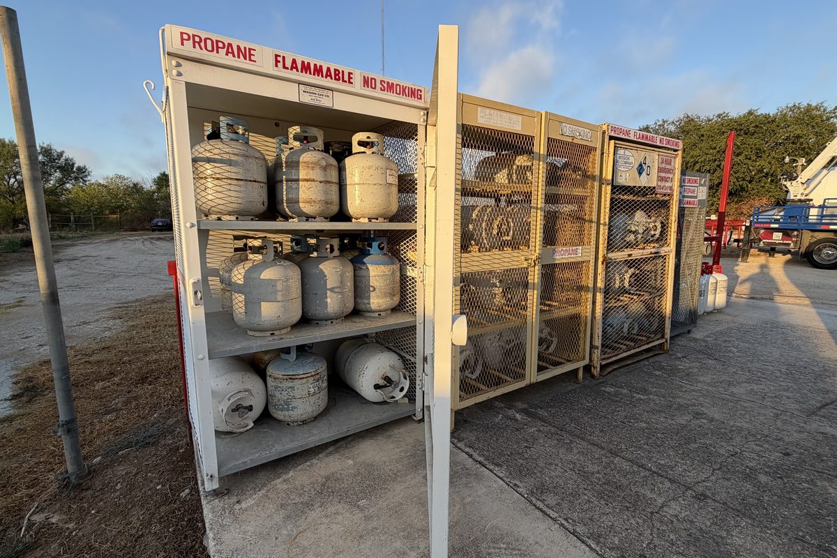 Outdoor propane tank storage cage with safety signage, Mission Gas Company truck parked nearby