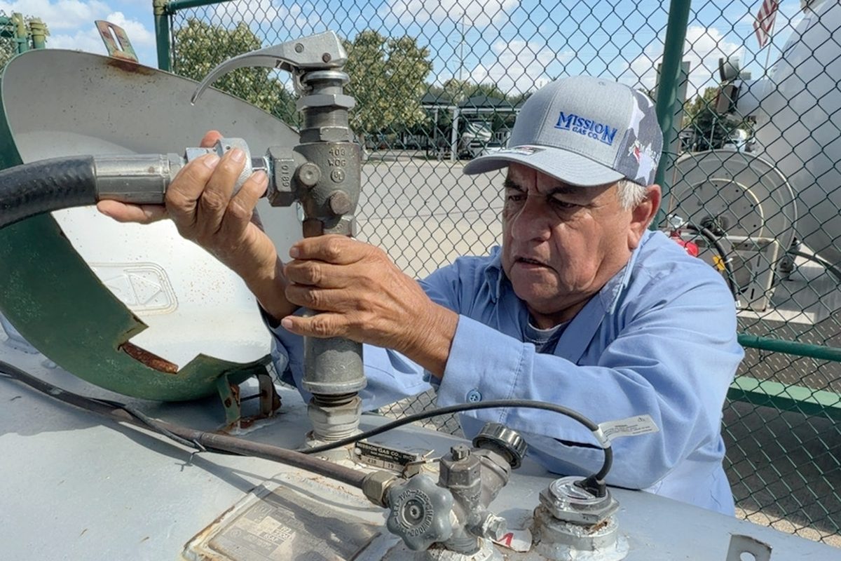 Technician wearing a Mission cap adjusts valves on top of a propane tank