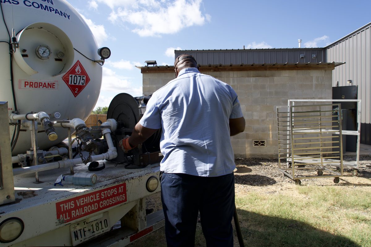Mission Gas Company technician connects hose to a propane delivery tanker truck outside a building