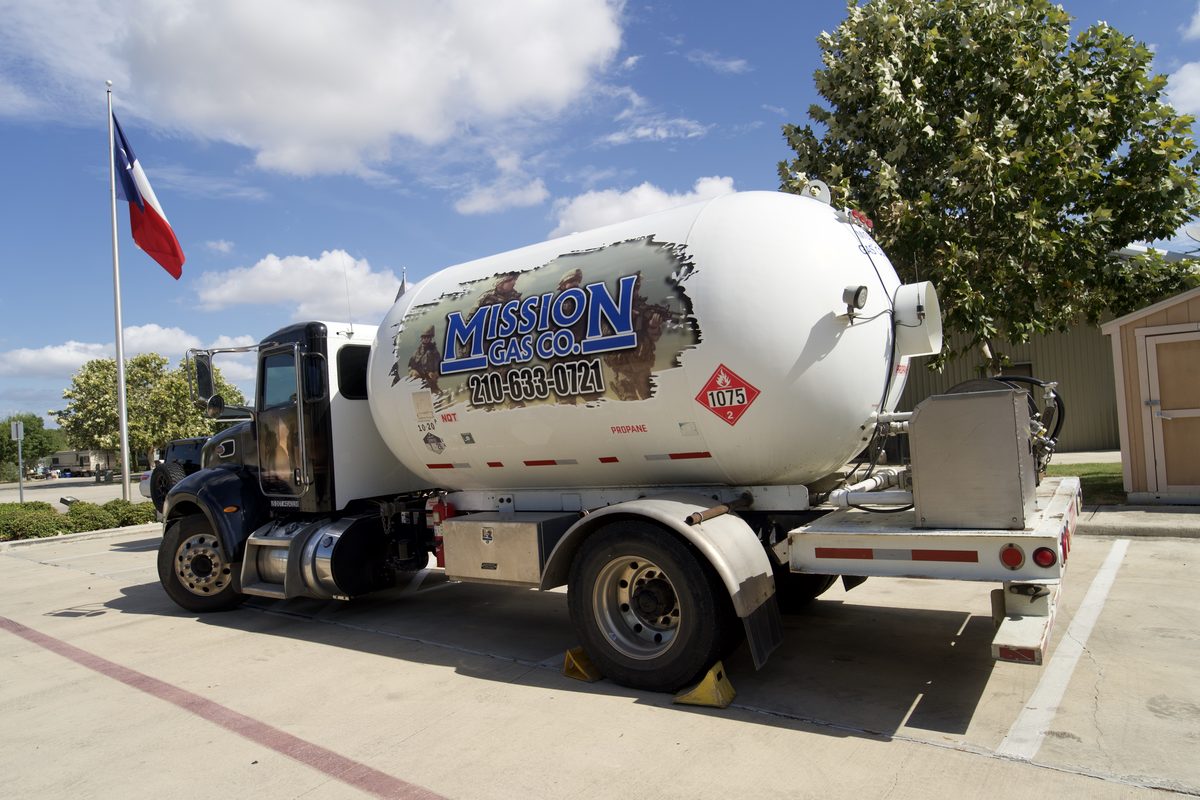 White propane tanker truck with Mission Gas Co. branding parked near a Texas flag