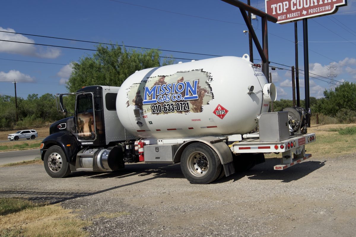 Mission Gas Co. propane tanker truck parked near a Top Country Meat Market sign under a blue sky