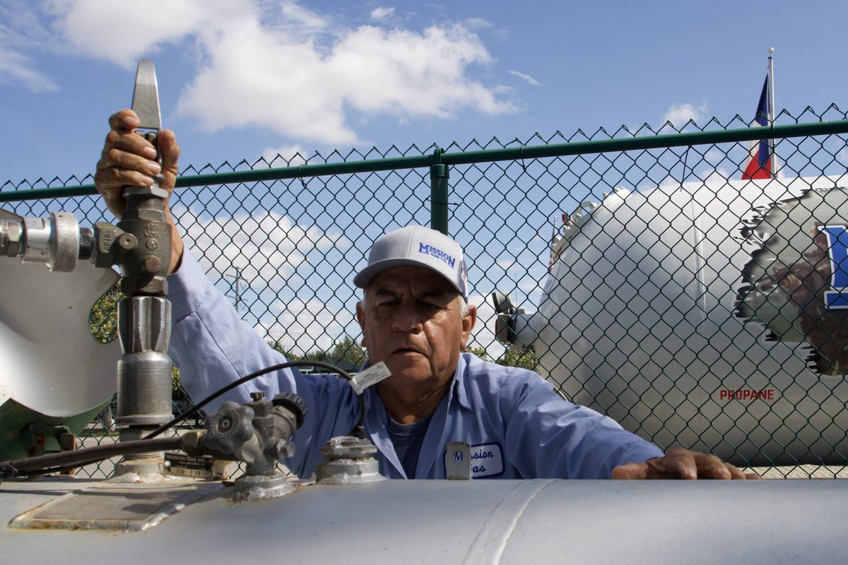 Worker in Mission Gas Co. uniform operating a valve on a propane tanker truck