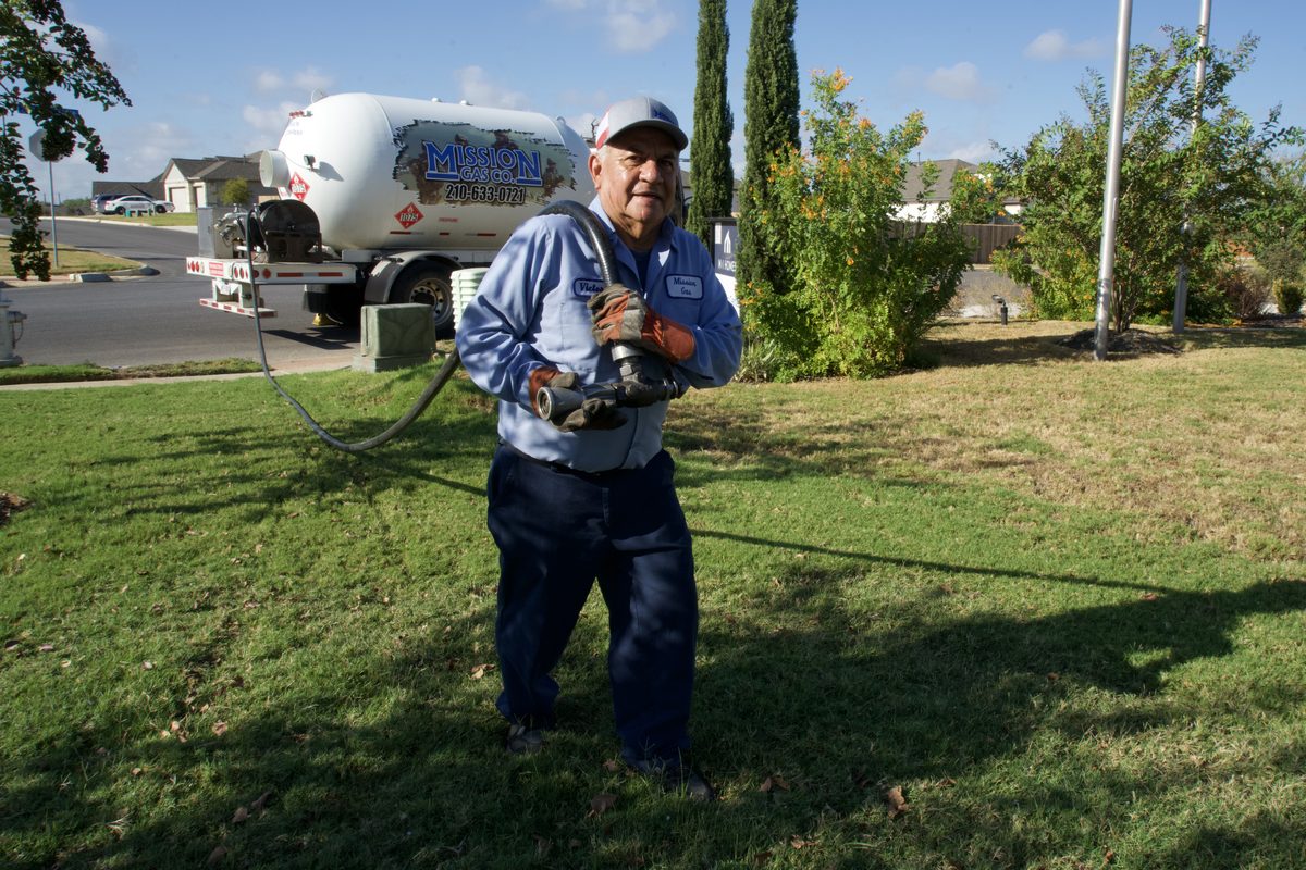Mission Gas Co. technician holds a fill hose beside a propane delivery truck on a lawn