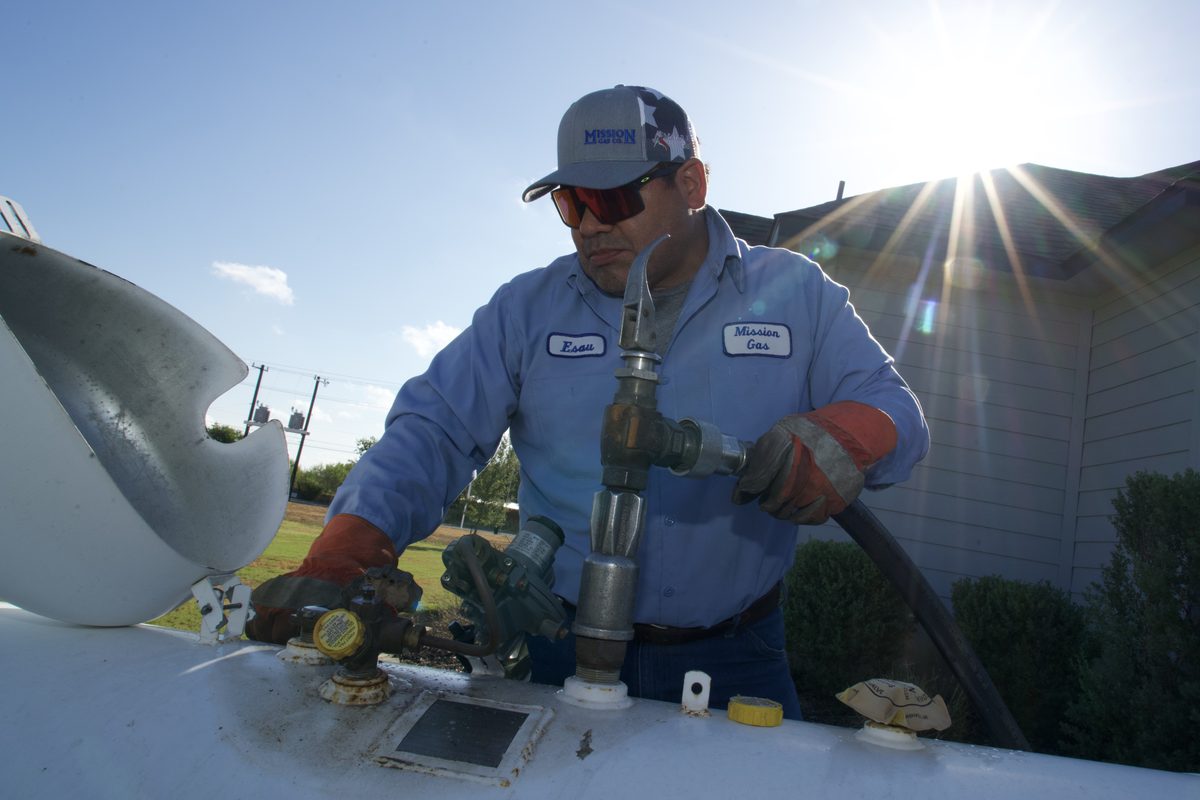 Mission Gas technician operates a propane fill valve on a tanker truck outdoors