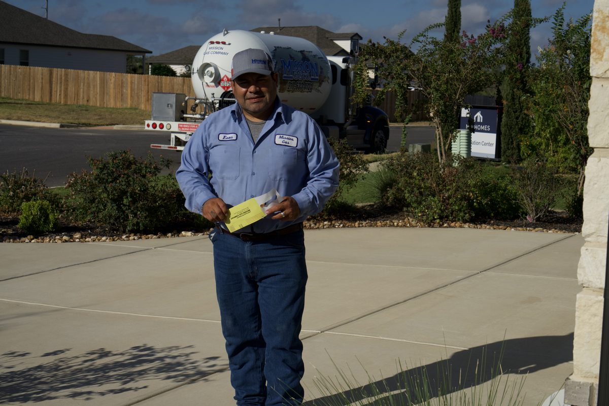 Mission Gas technician in uniform holding paperwork beside a propane delivery truck