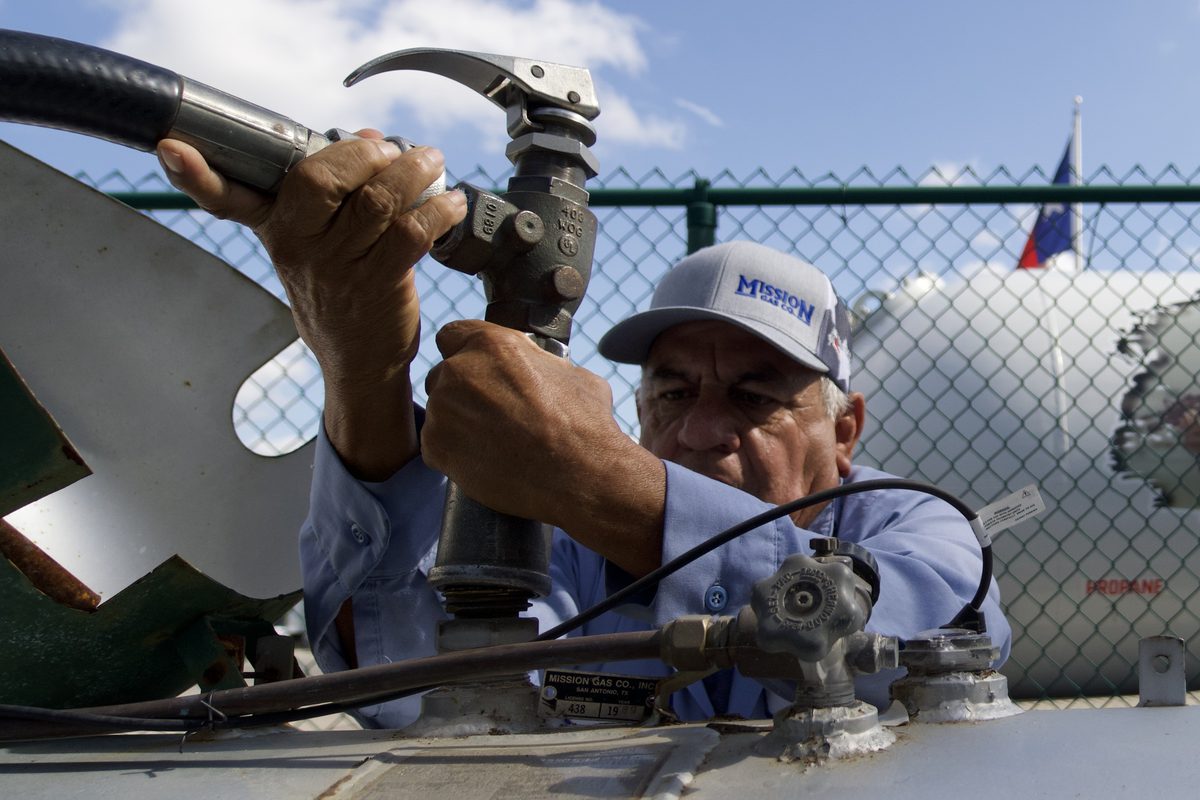 Technician in Mission cap turns a valve on top of a propane tank, another tank labeled Mission Gas behind