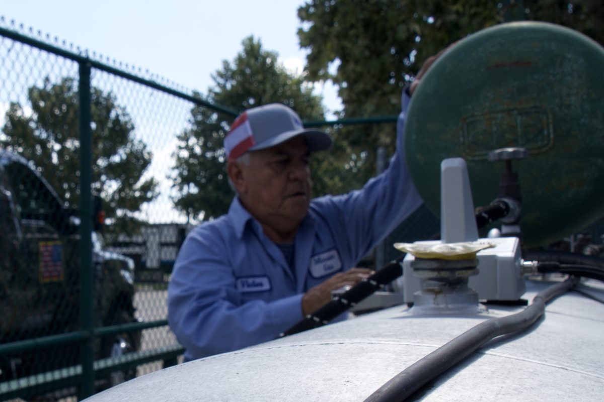 Technician in uniform checking a valve on top of a large propane tank outdoors