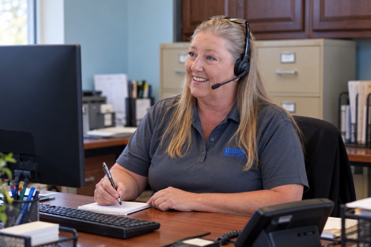 Smiling Mission Gas customer service representative in a headset taking notes at her desk