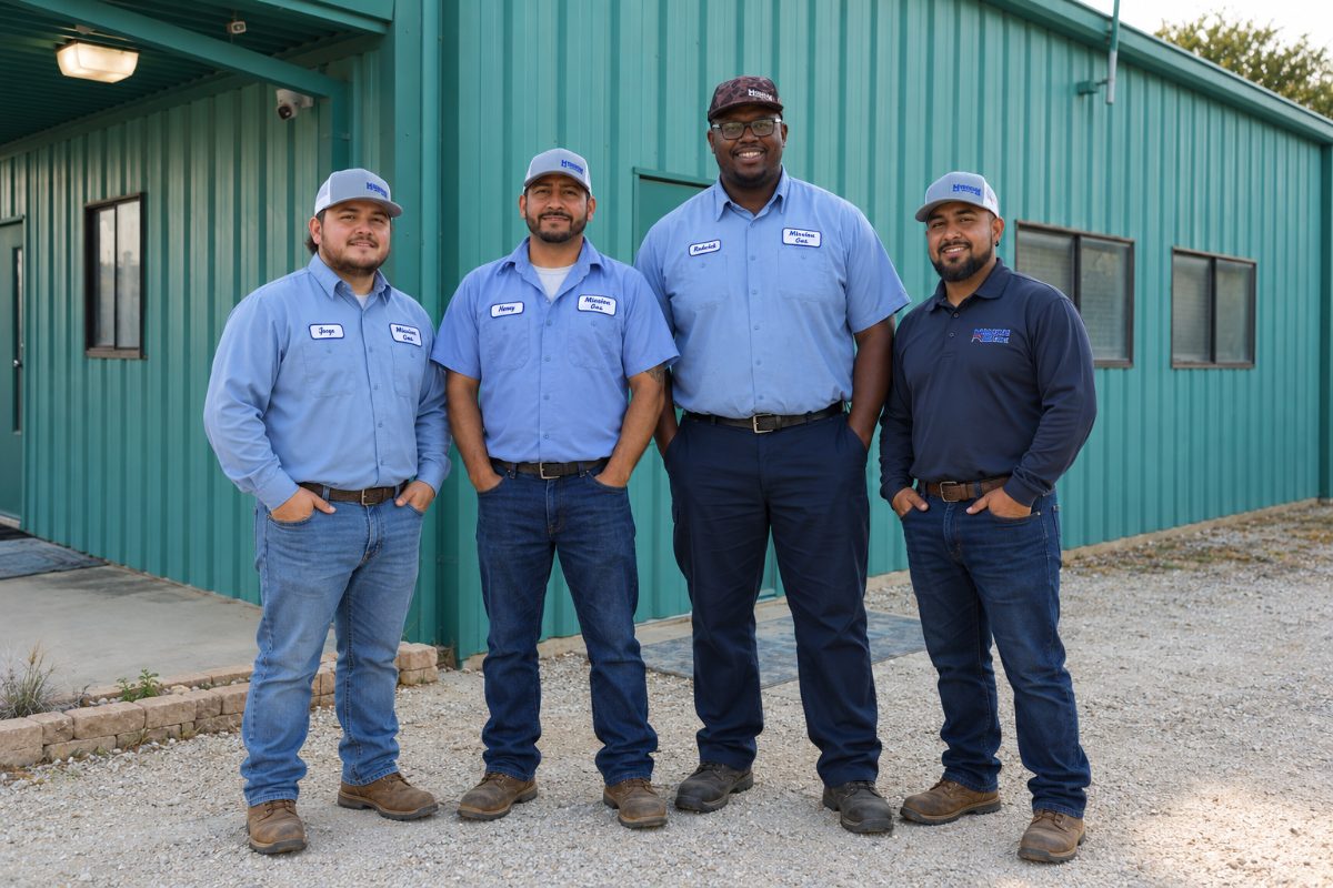 Four Mission Gas team members in uniform standing outside a green metal workshop