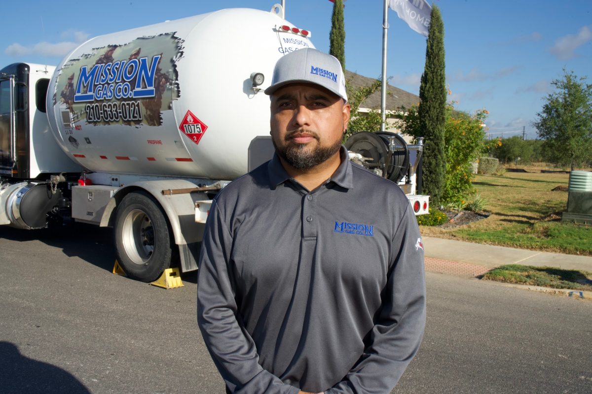 Mission Gas driver in a gray polo and cap standing in front of a Mission Gas propane delivery truck