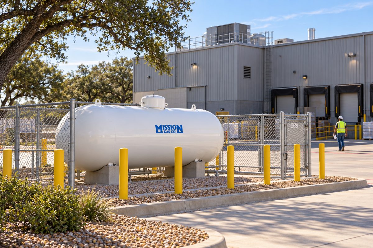 Mission Gas propane storage tank inside a fenced enclosure with safety bollards at an industrial facility