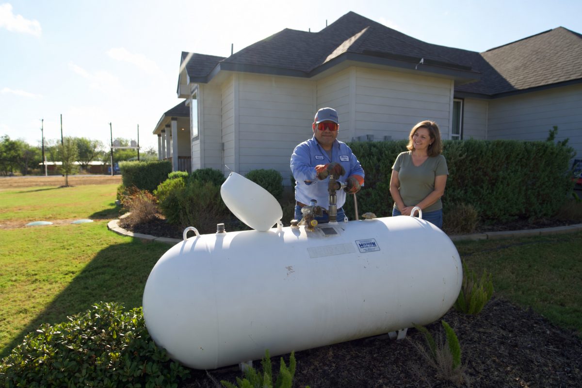 Mission Gas technician checking the gauge on a residential propane tank while the homeowner looks on