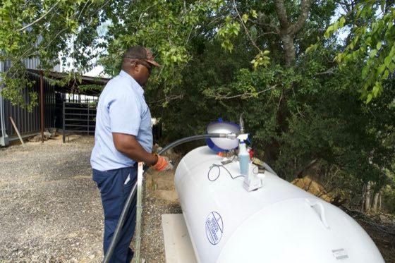 Mission Gas technician checking a propane tank under shade trees on a South Texas ranch